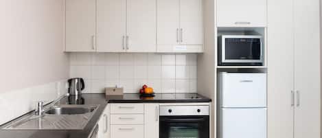 A modern kitchen with white cabinets, a black countertop, a stainless steel sink, a microwave, and a built-in oven.