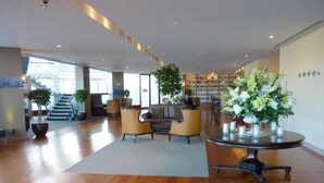 A spacious lobby with a wooden floor, seating area with armchairs, a coffee table, and a large bookshelf. - The Spencer Suites By Castle (Auckland)