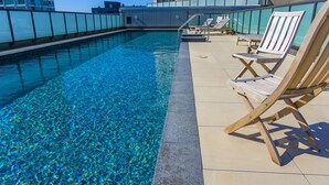 A rooftop pool with clear blue water, wooden lounge chairs, and a glass railing. - The Spencer Suites By Castle (Auckland)