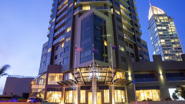 A multi-story hotel with a prominent corner entrance, large windows, and a well-lit facade. - The Spencer Suites By Castle (Auckland)