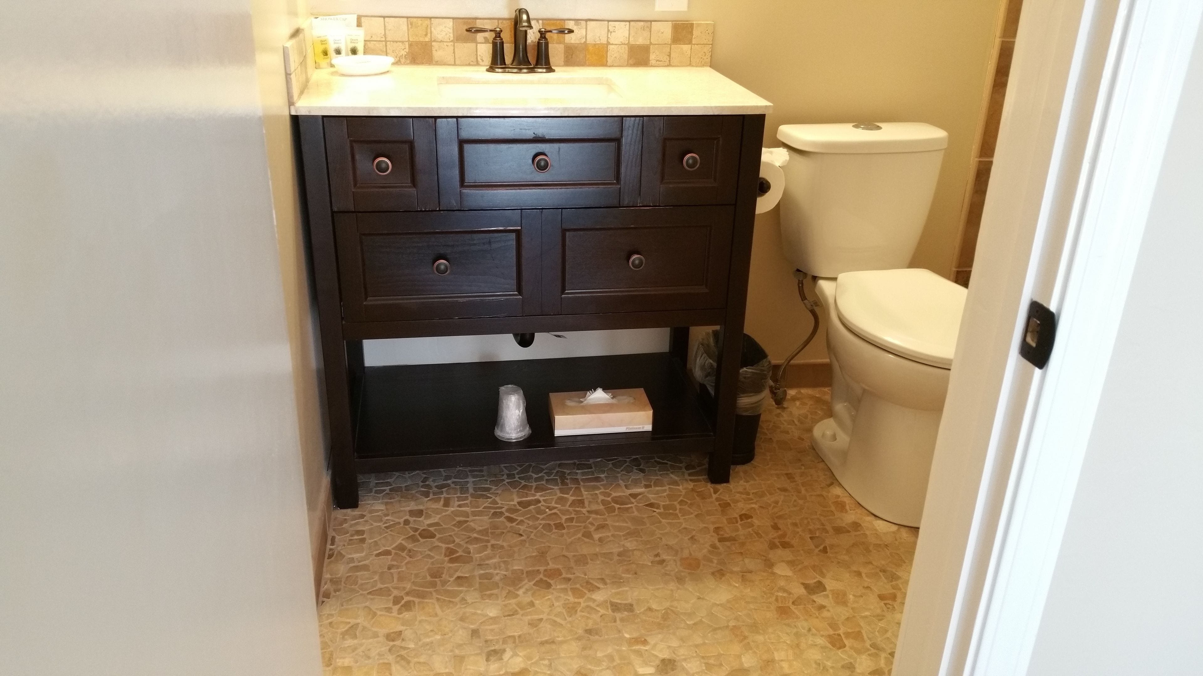 Un baño con tocador de madera oscura, inodoro blanco y piso de baldosas.