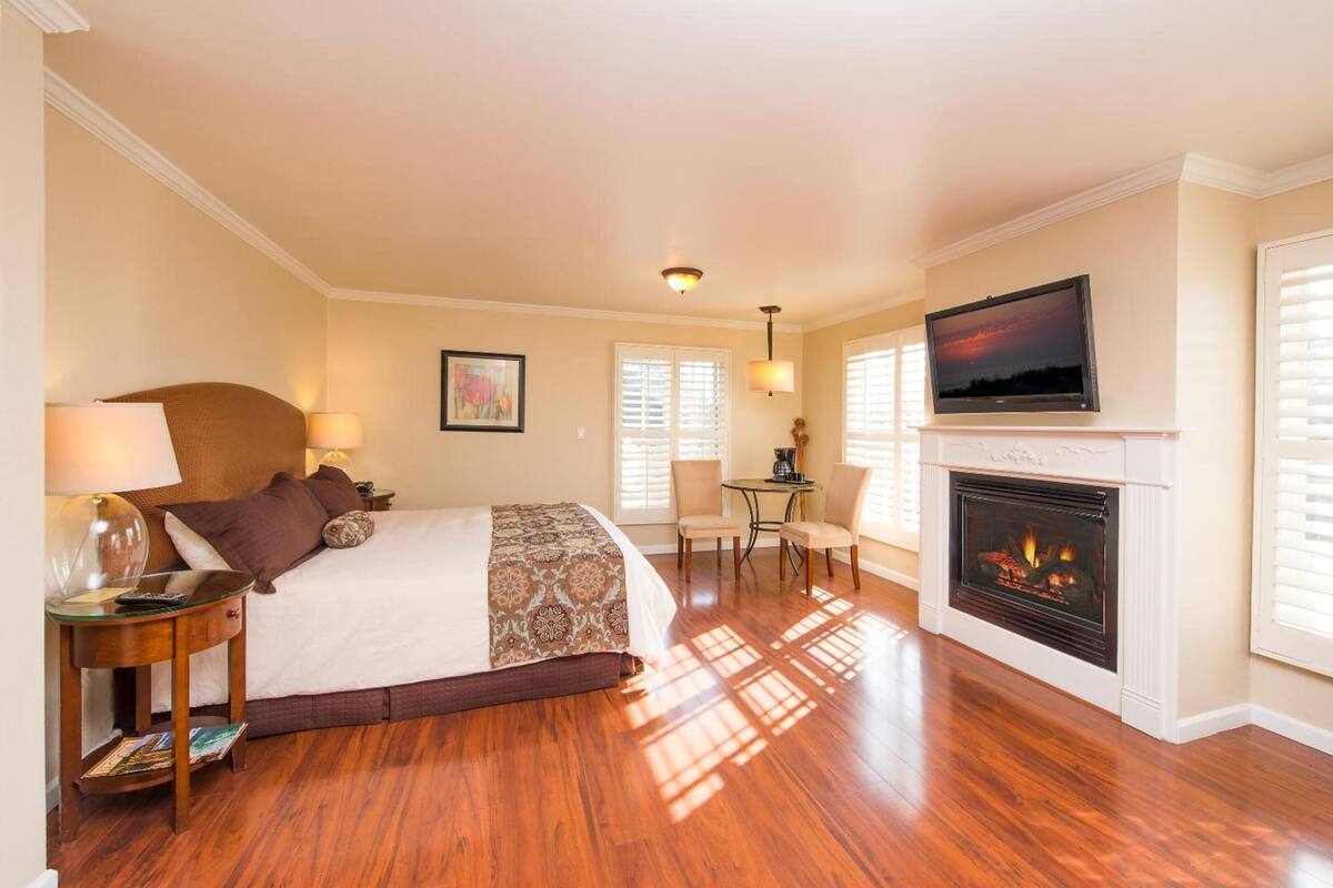 Quarto de hotel com uma cama grande, lareira, televisão e uma pequena mesa com cadeiras.