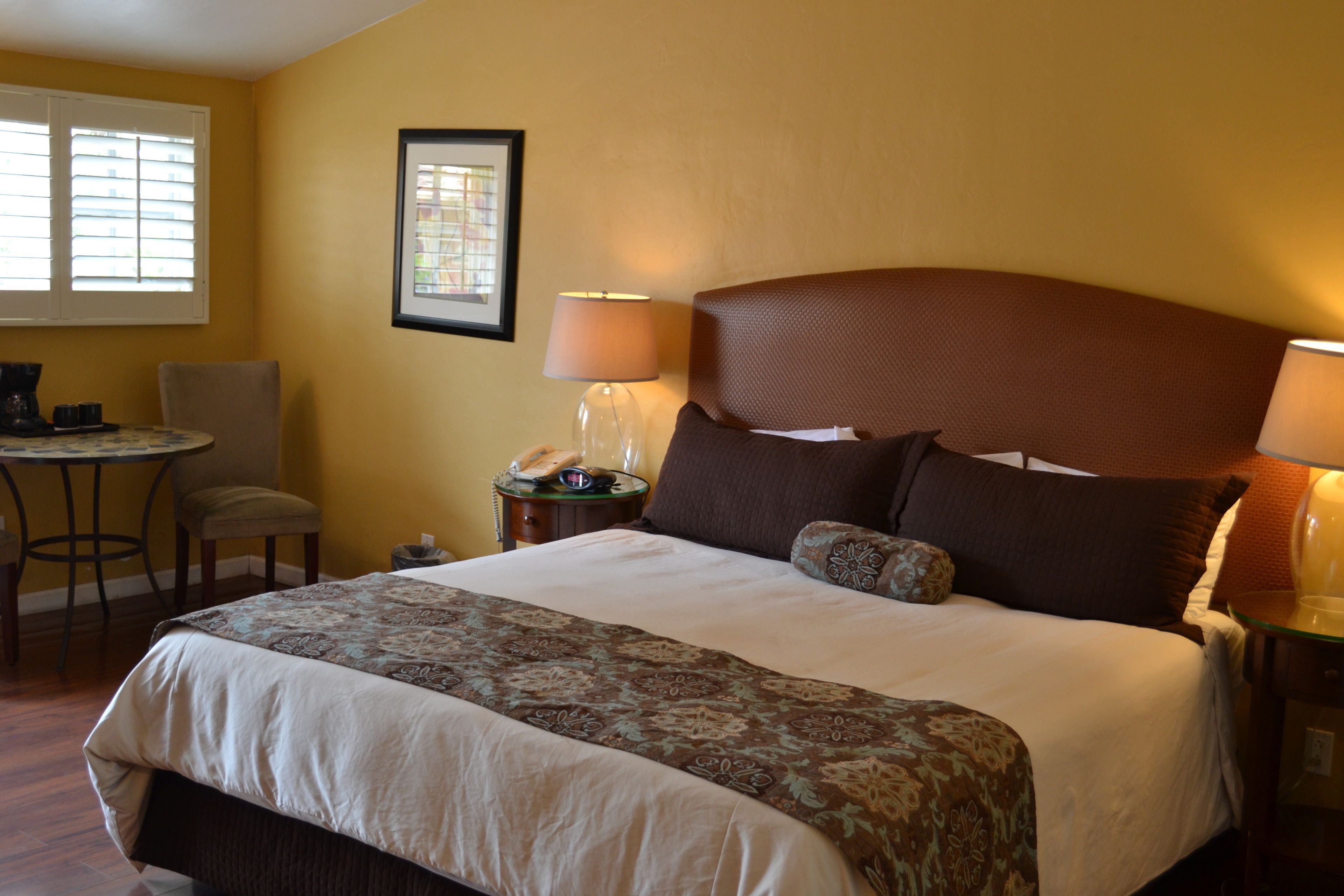 A hotel room with a large bed, a desk with a chair, a lamp, and a framed picture on the wall.