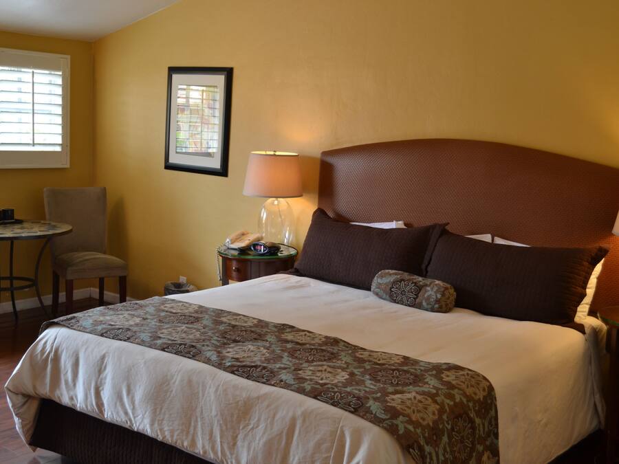 A hotel room with a large bed, a desk with a chair, a lamp, and a framed picture on the wall.