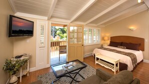 A bedroom with a bed, a TV, a glass coffee table, a bench, and a door leading to a balcony. - Sunset Inn (Pacific Grove)