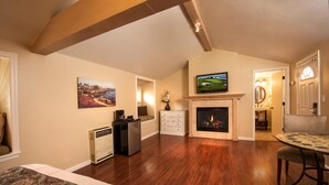A spacious living room with hardwood flooring, a fireplace, a television, and a dining area with a round table. - Sunset Inn (Pacific Grove)