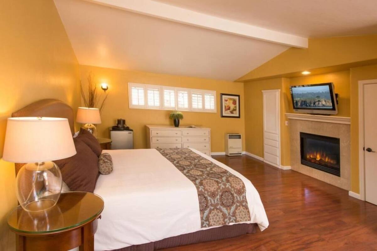 Quarto com cama, televisão, lareira e mesa de cabeceira com abajur.