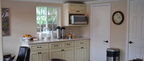 A kitchen with white cabinets, a microwave, a trash can, and a clock on the wall.