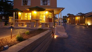 A two-story building with a covered patio area, stone planters, and outdoor lighting. - Sunset Inn (Pacific Grove)