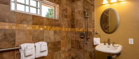Un bagno con doccia, lavandino, specchio e porta asciugamani.
