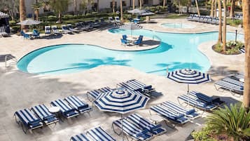 Zwembadgedeelte van een resort met ligbedden en parasols, omringd door palmbomen en een gebouw met balkons.