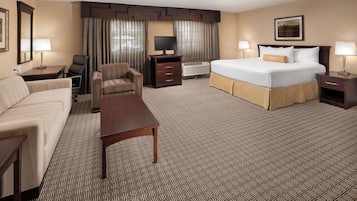 Quarto de hotel com cama, escrivaninha, cadeira, televisão e janela com cortinas.
