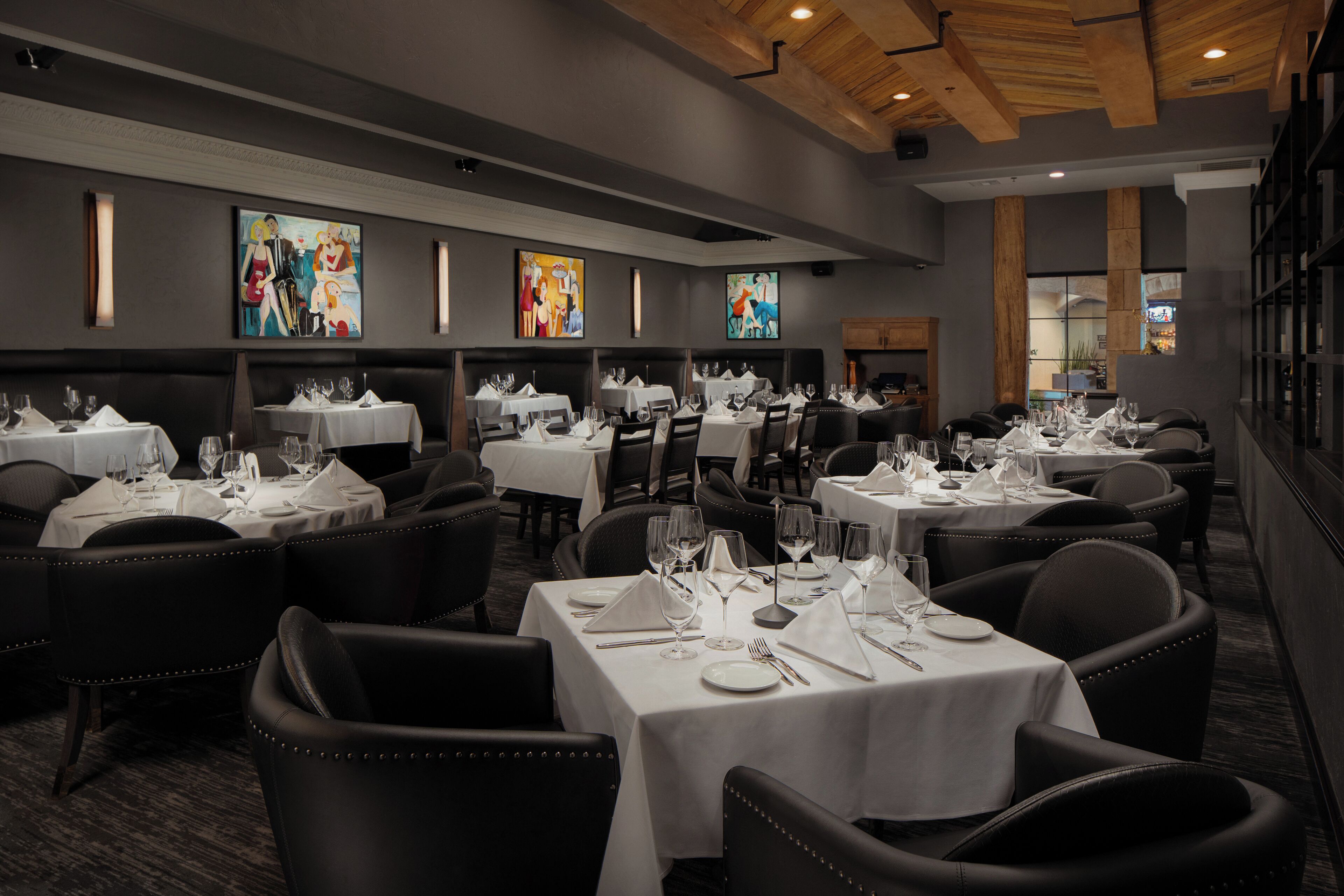 Een restaurant met meerdere tafels voor diners, met een modern interieur, houten balken in het plafond en kunstwerken aan de muren.