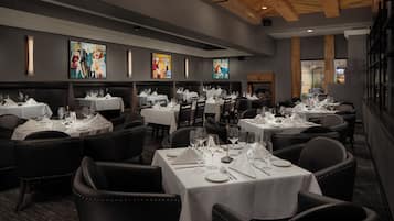 Een restaurant met meerdere tafels voor diners, met een modern interieur, houten balken in het plafond en kunstwerken aan de muren.