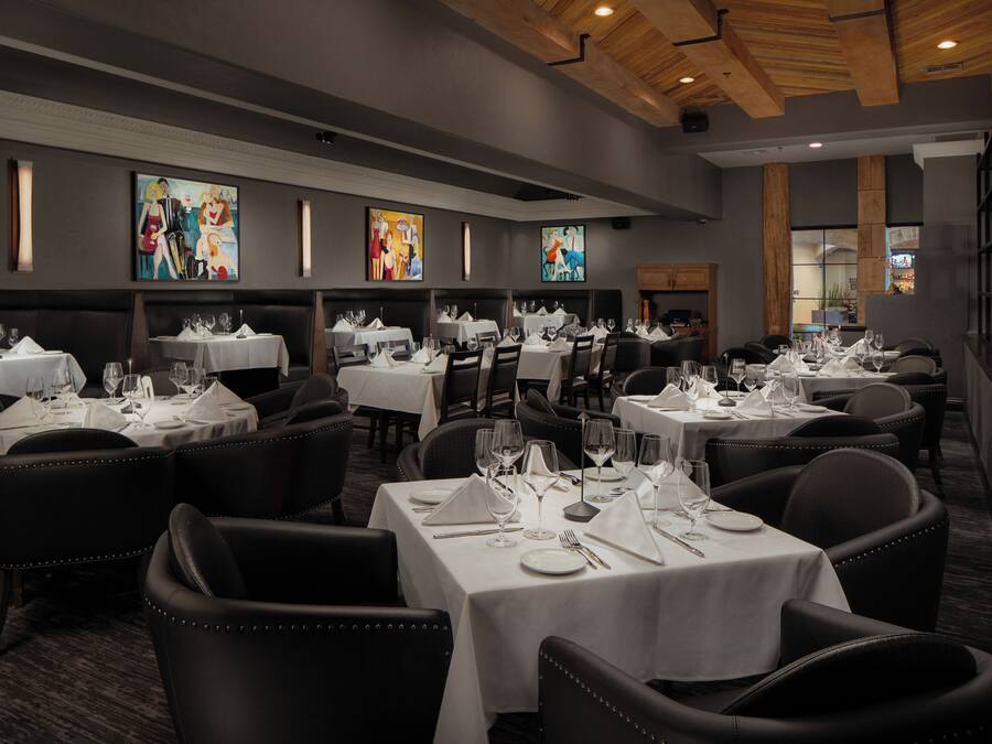 Een restaurant met meerdere tafels voor diners, met een modern interieur, houten balken in het plafond en kunstwerken aan de muren.