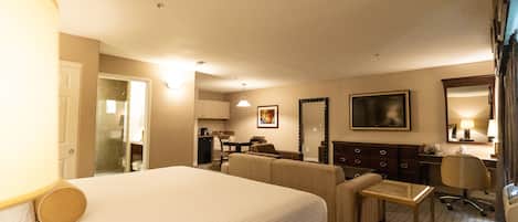 Una habitación de hotel con una cama grande, un escritorio, una silla, un sofá, una mesita y un espejo.
