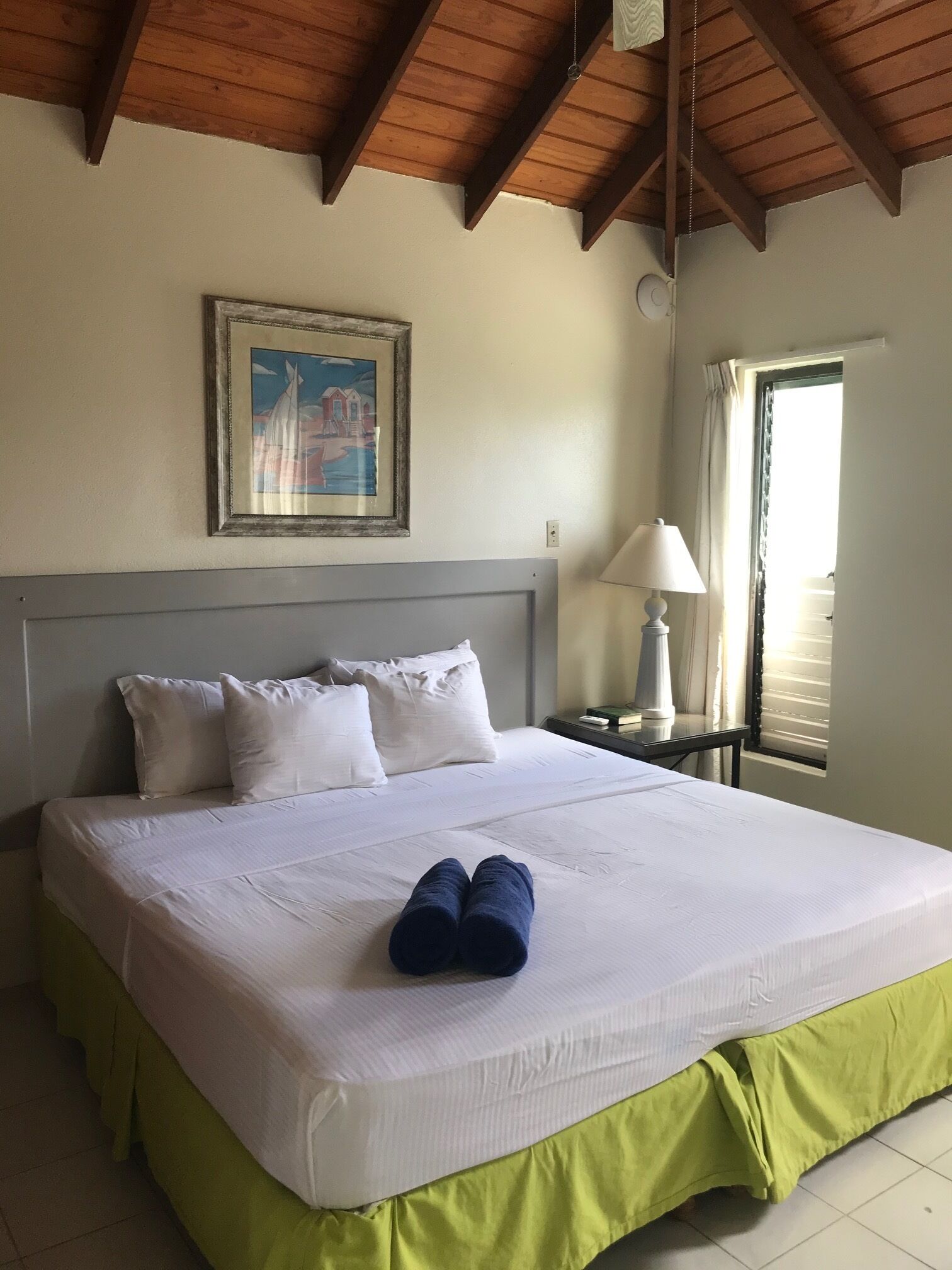 A hotel room with a large bed, a framed picture on the wall, a bedside table with a lamp, and a window with curtains.