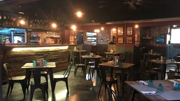 Un restaurante con área de bar, mesas, sillas y una barra.