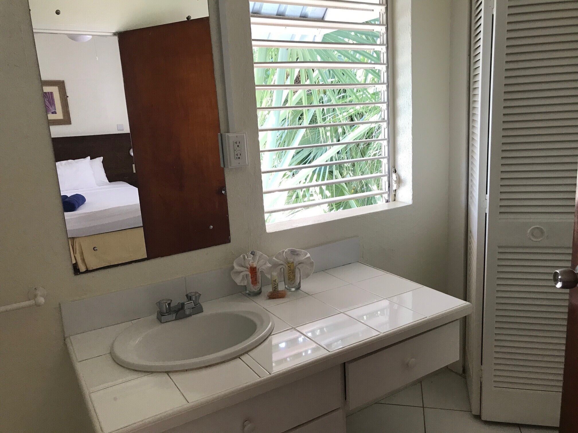 Ein Badezimmer mit einem weißen Waschbecken, einem Spiegel und einem Fenster mit Jalousien.