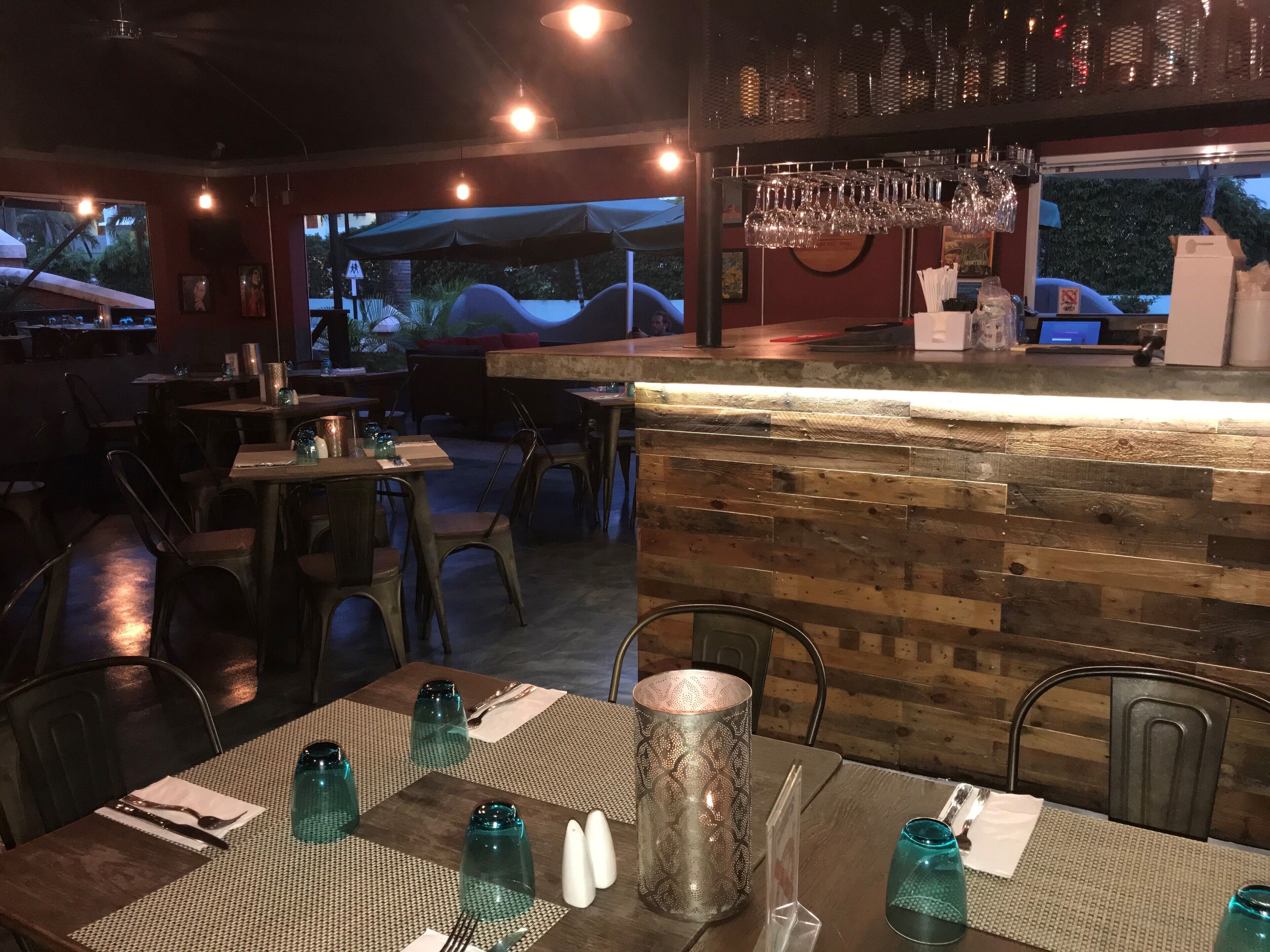 Ein Restaurant mit einer rustikalen Holztheke, Tischen mit blauem Glas und Blick ins Freie.