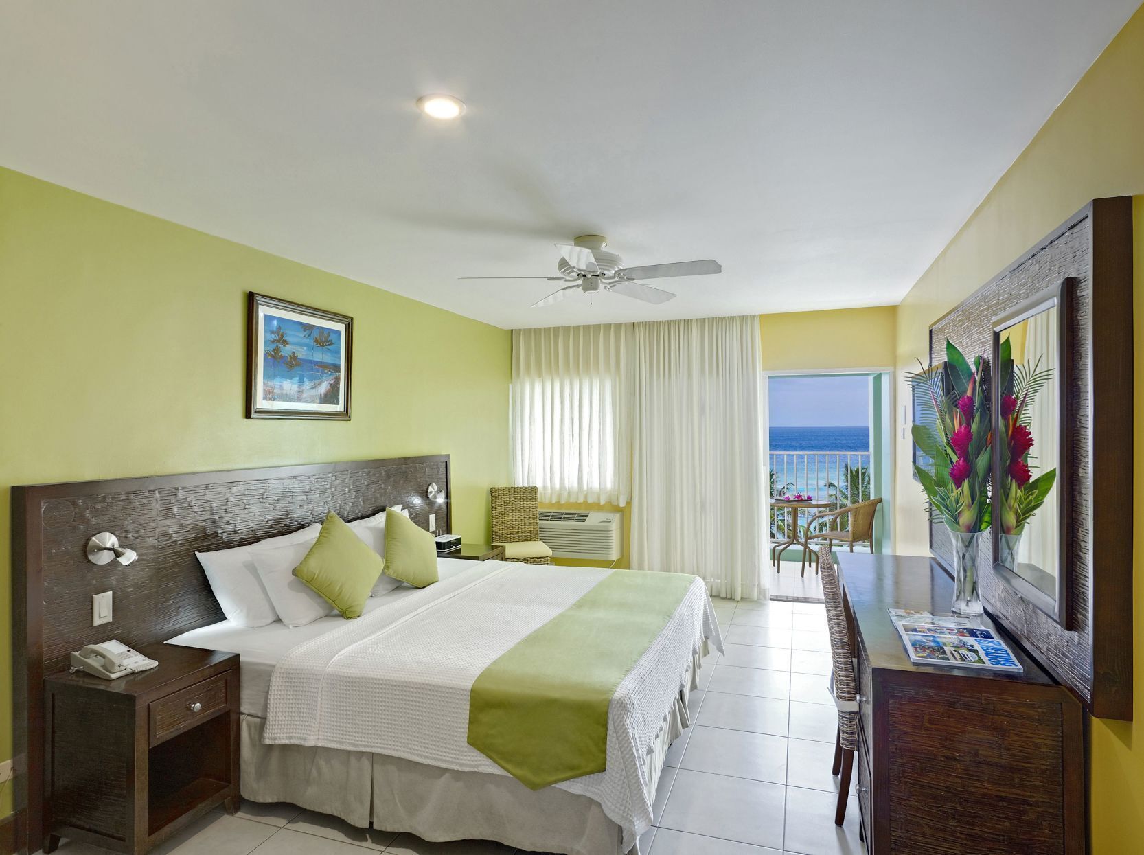Ein Hotelzimmer mit Bett, Schreibtisch, Stuhl, Deckenventilator und Meerblick.