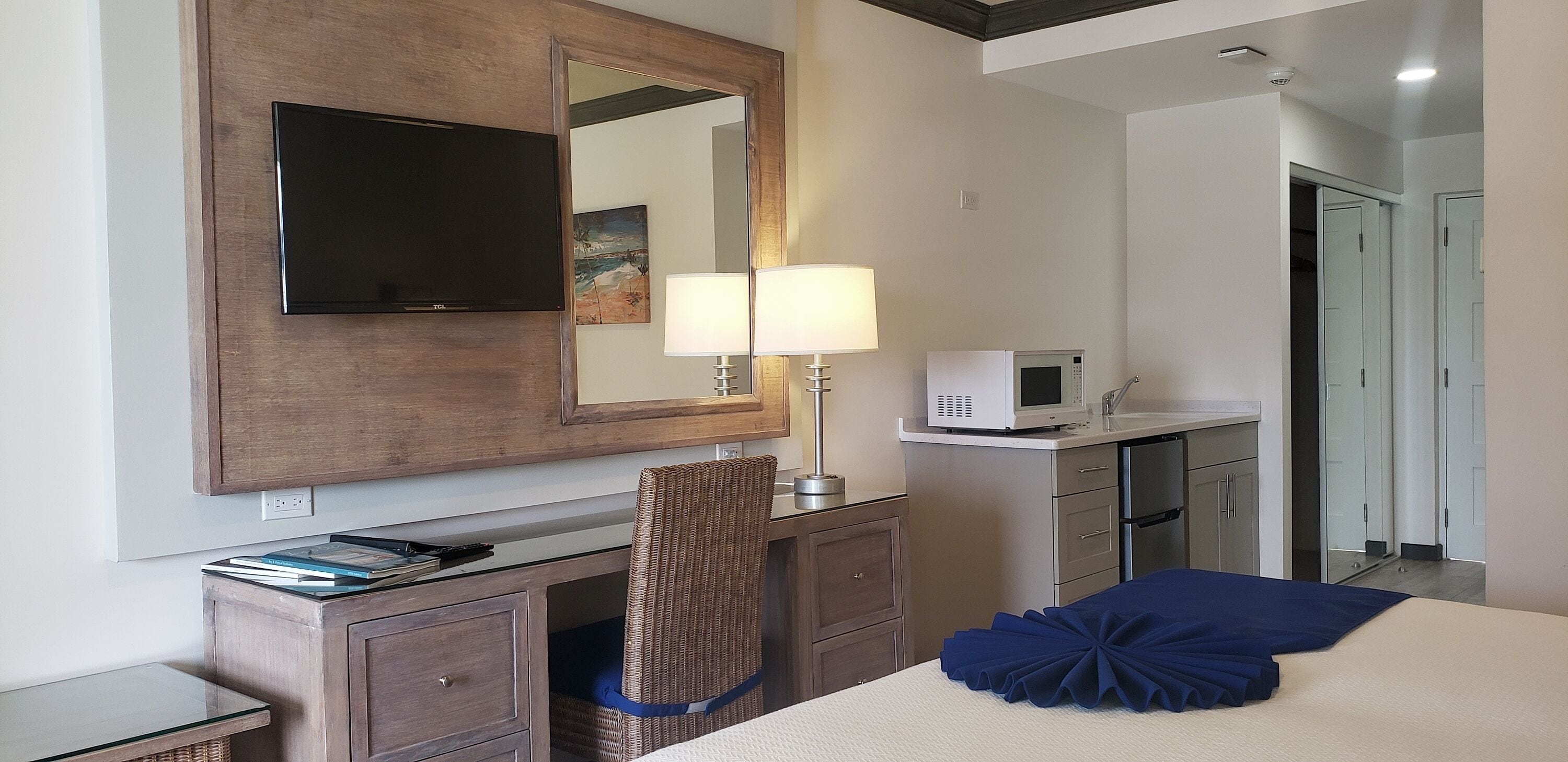 Una habitación de hotel con una cama, un escritorio con lámpara, un televisor, un microondas y un armario.