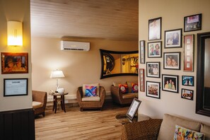 A cozy living room with wicker furniture, a wall-mounted air conditioner, and various framed photos.