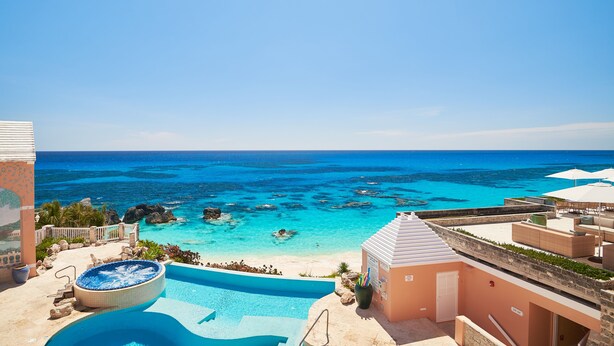 A resort pool with a hot tub, a beach view, and a clear blue sky.