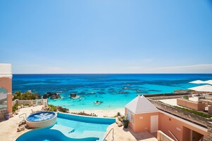 Una piscina de resort con un jacuzzi, vista a la playa y un cielo azul despejado.