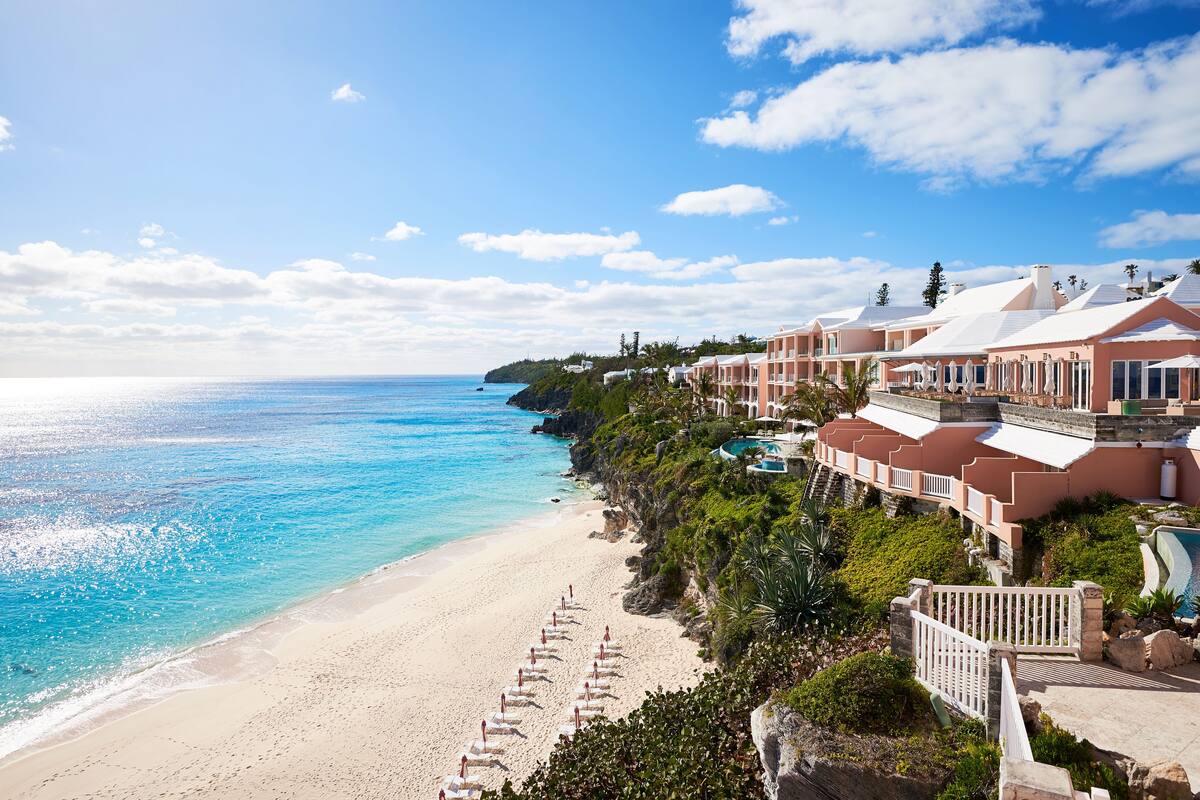 A beachfront hotel with a long sandy beach, multiple swimming pools, and a clear view of the ocean.