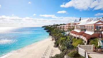 A beachfront hotel with a long sandy beach, multiple swimming pools, and a clear view of the ocean.