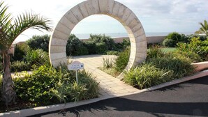 A stone archway with a cycle parking sign, surrounded by greenery and a view of the sea.