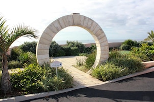 Un arco de piedra con un cartel de estacionamiento para bicicletas, rodeado de vegetación y vistas al mar.