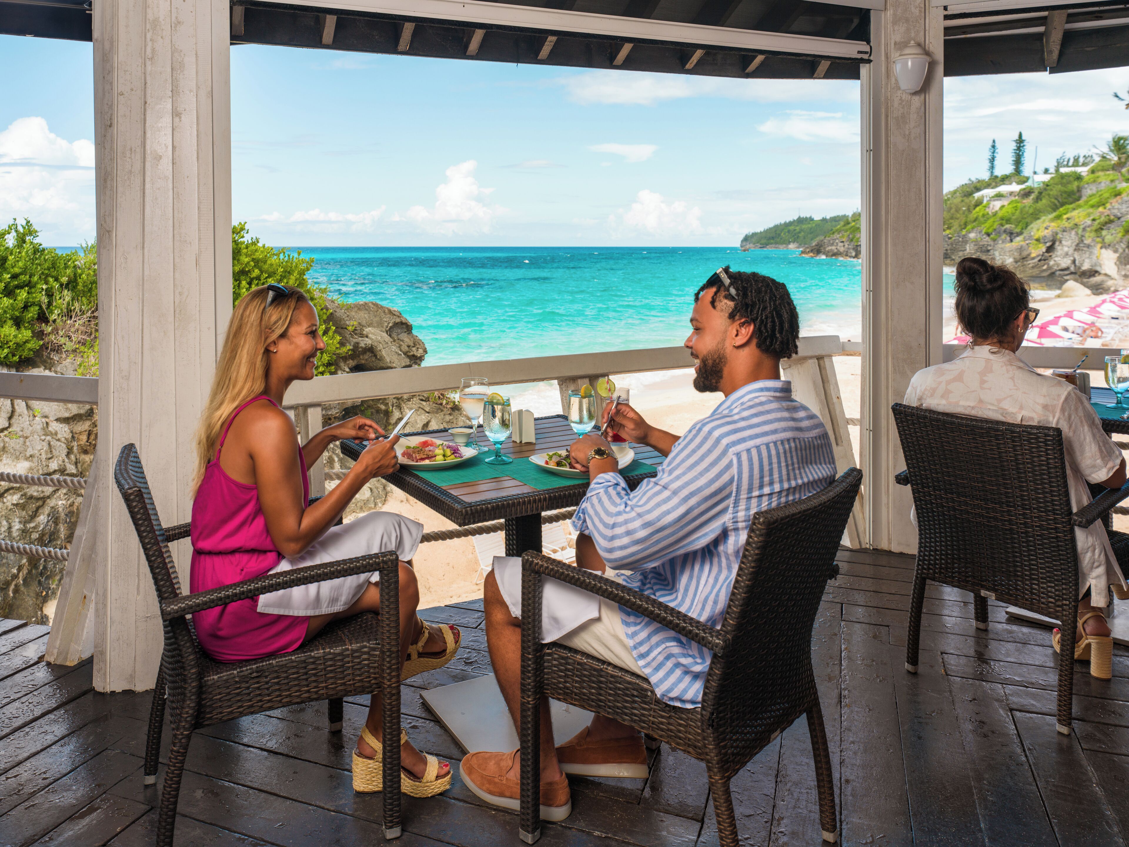A covered outdoor dining area with wicker furniture and a view of the ocean.