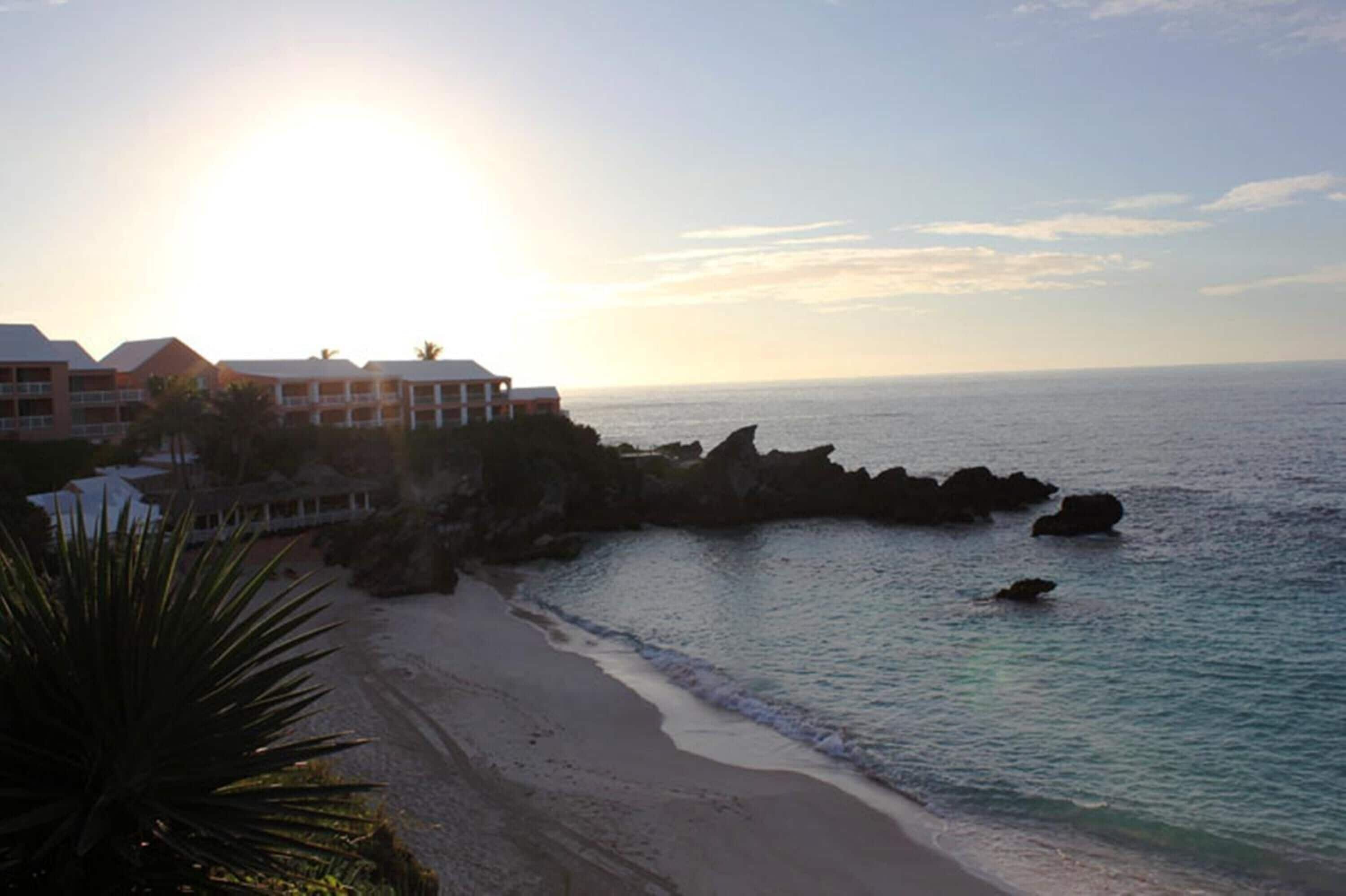 Un hotel frente a la playa con vistas al océano, una playa de arena y formaciones rocosas.
