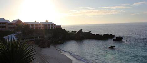 Un hotel frente a la playa con vistas al océano, una playa de arena y formaciones rocosas.