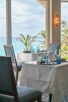 Mesa de comedor con vajilla azul y un cuadro enmarcado, con vista a una playa con palmeras.