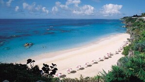 A beach with clear turquoise waters, a sandy shore, and a row of umbrellas.