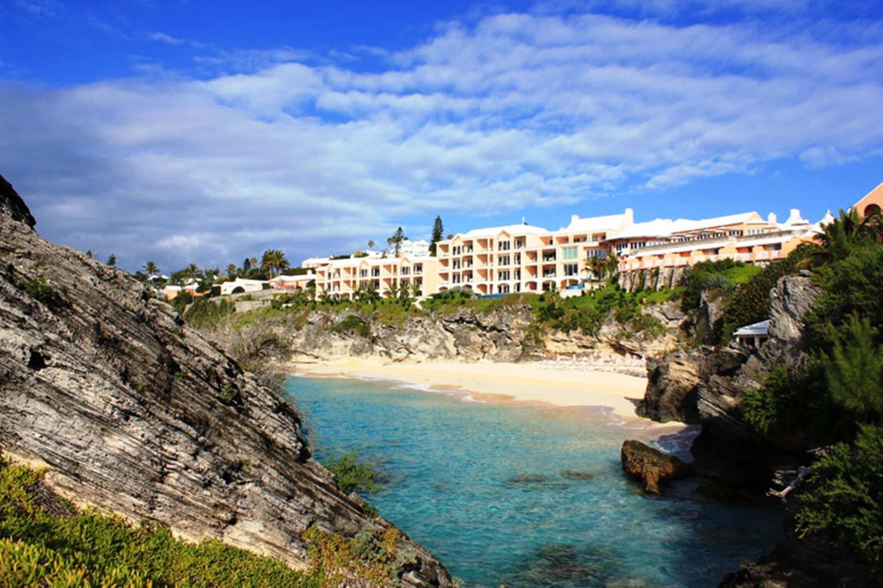 Un hotel frente al mar con varias construcciones, un litoral rocoso y aguas azul turquesa.