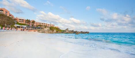A beach with a resort building, clear skies, and calm sea.