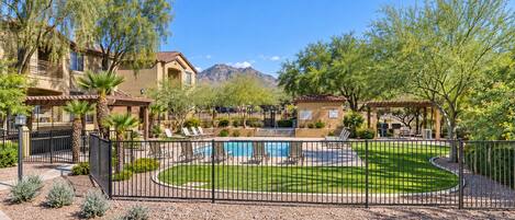 A residential area with a swimming pool, fenced yard, and mountain views.