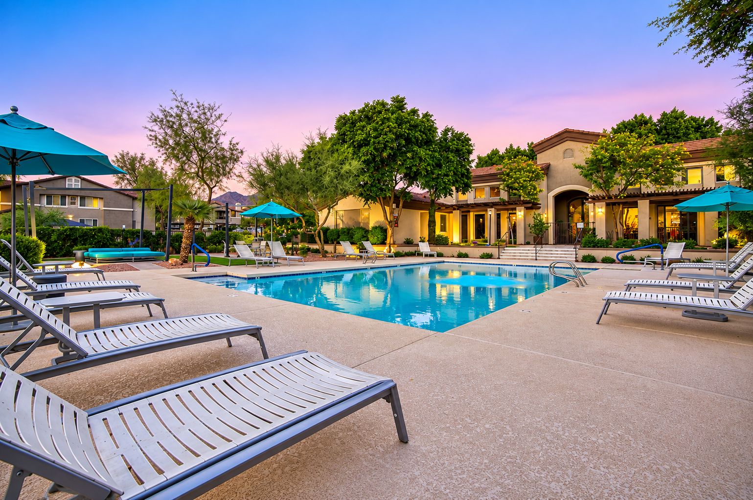A swimming pool with lounge chairs and umbrellas, surrounded by buildings with a warm color palette.