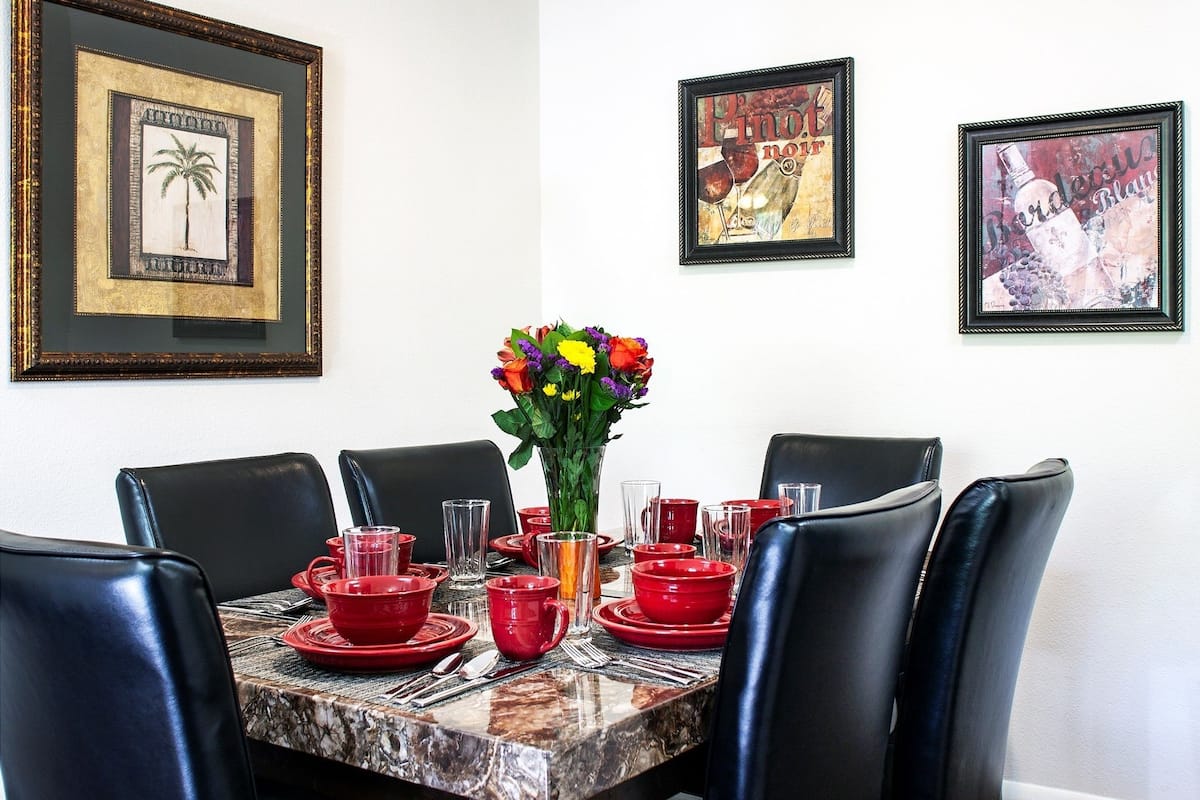 A dining table with red and clear glassware, black chairs, and a vase with flowers.