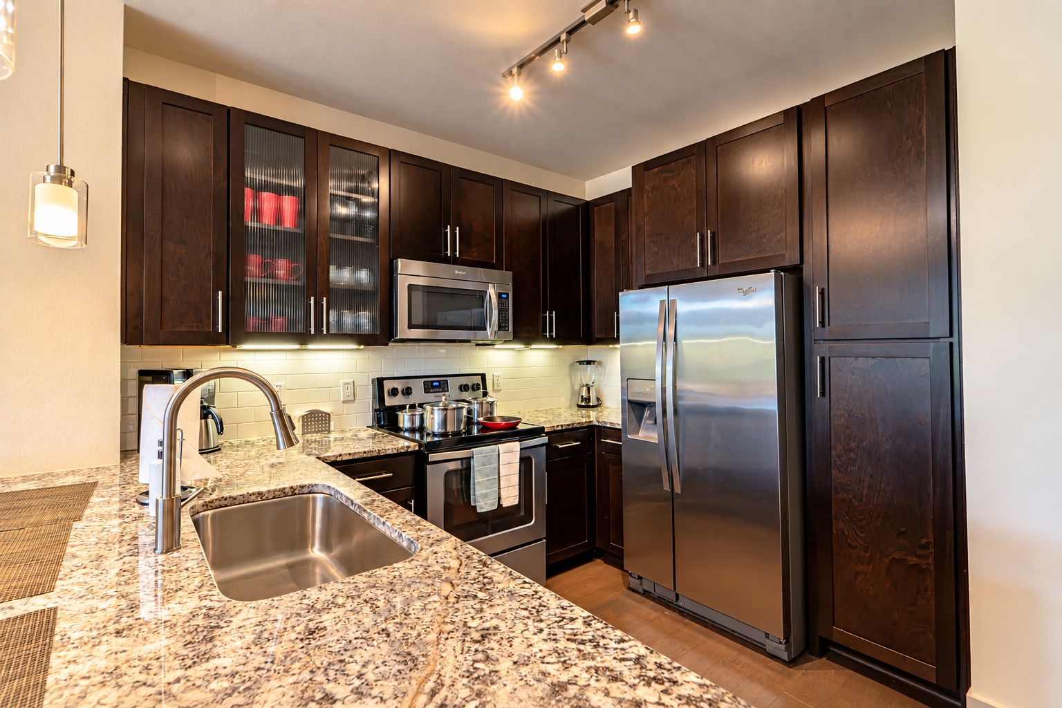 A modern kitchen with dark wood cabinets, stainless steel appliances, and a granite countertop.