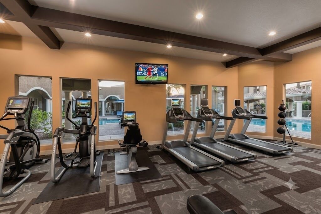 A gym with treadmills, elliptical machines, and a television screen displaying a sports event.