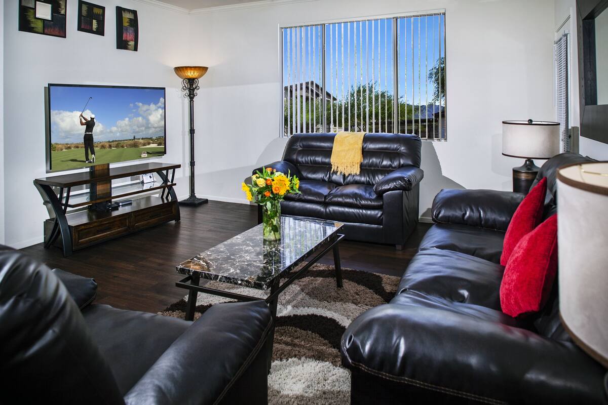 A living room with a TV, a black leather sofa, a coffee table, and a lamp.