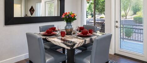 A dining area with a marble table, grey chairs, red tableware, and a vase of flowers.