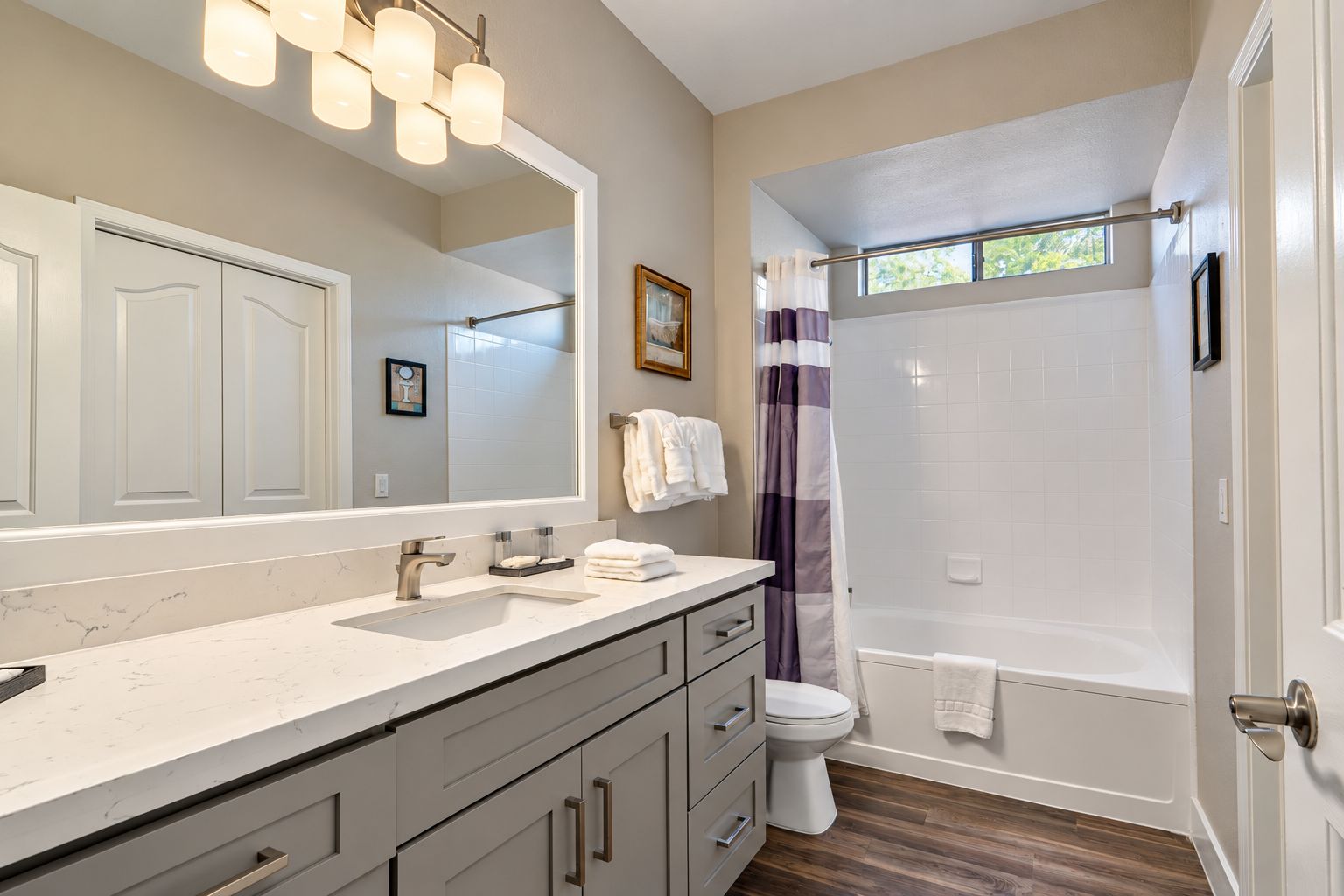 A bathroom with a large mirror, a sink, a toilet, and a shower area.