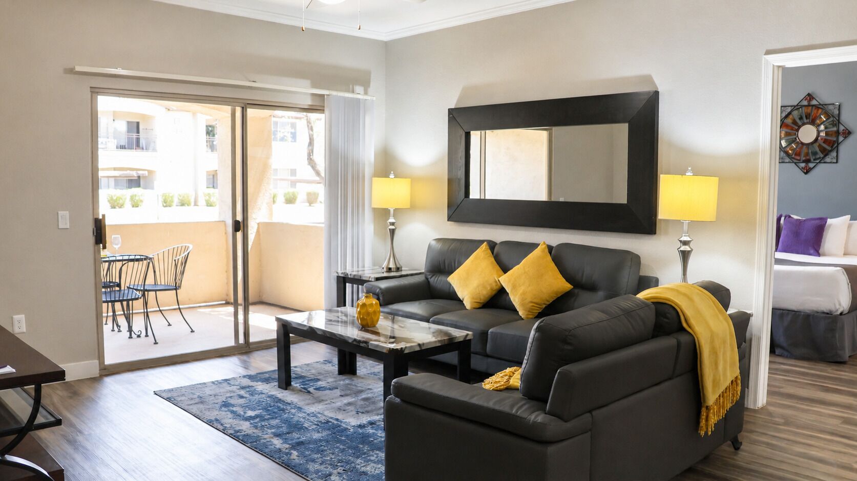 Uma sala de estar com sofá, mesa de centro e vista para uma área externa com mesa e cadeiras.