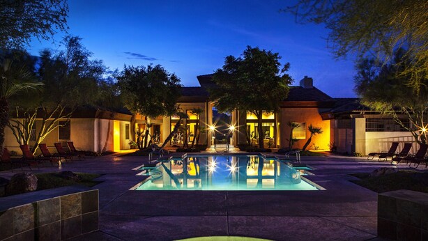 A pool area with lounge chairs and a building in the background. - Meridian CondoResorts (Scottsdale)